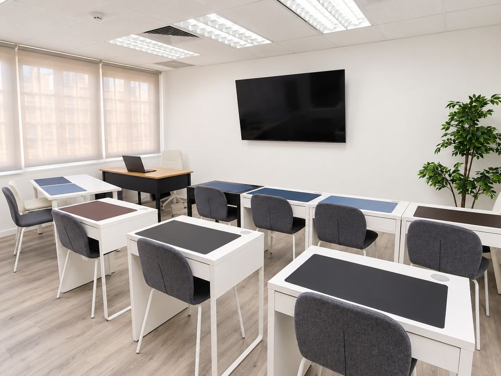 Bright main study hall with individual desks, a wall-mounted screen and window blinds